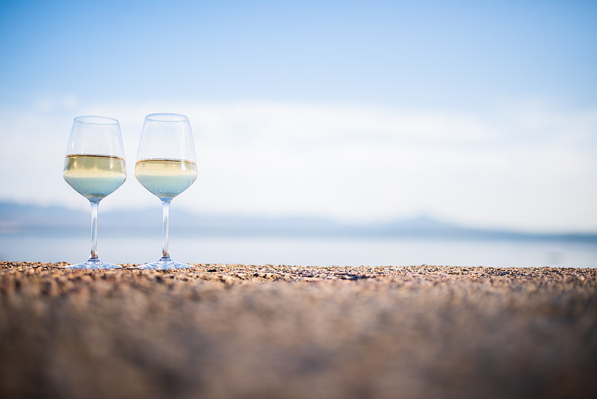 Two glasses of white wine on a stone wall overlooking the sea