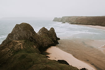 Misty coastal landscape with rocky cliffs and sandy beach
