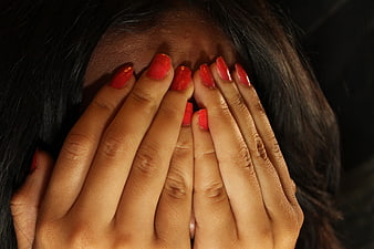 Close-up of woman covering face with hands and red nails