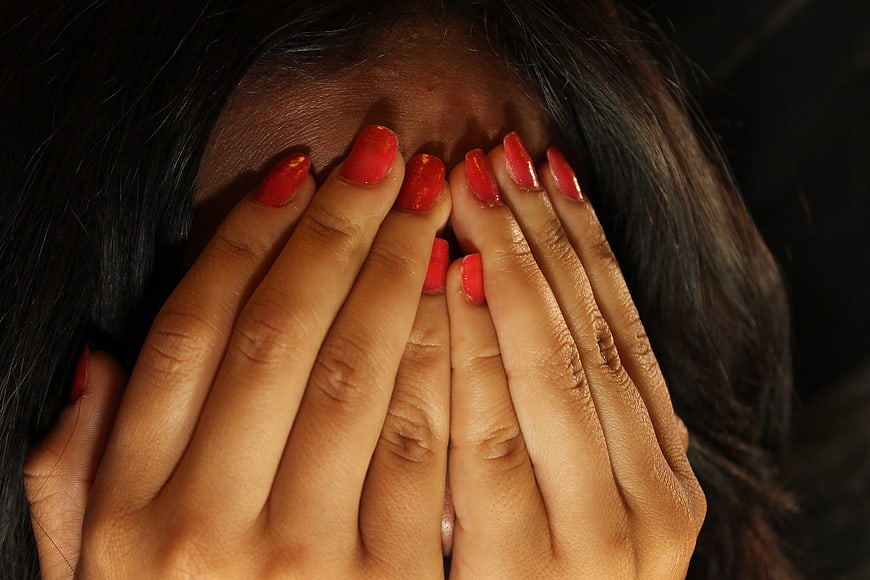 Close-up of woman covering face with hands and red nails