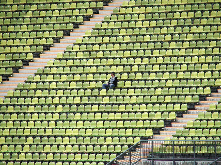 Lone man sitting in rows of empty green stadium seats