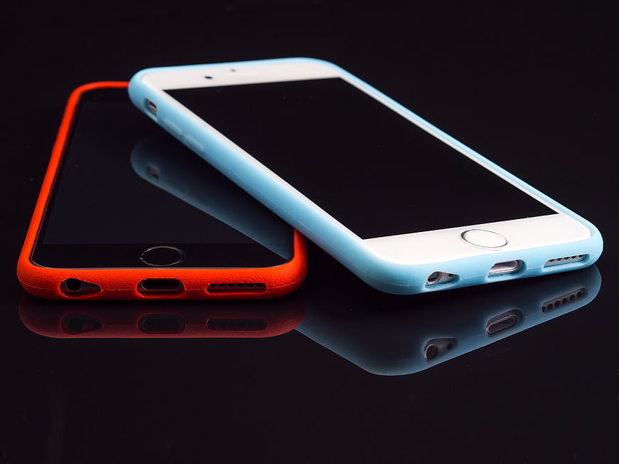 Two smartphones with colorful cases on reflective black surface