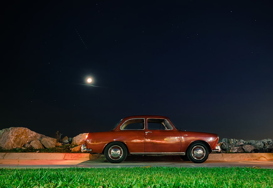 Vintage Red Car Parked Under Moonlit Night Sky