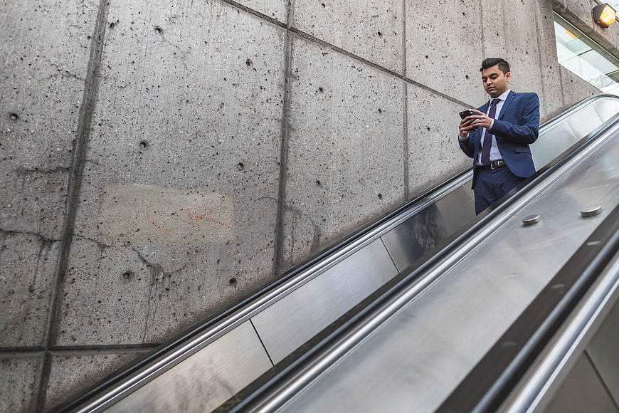 Businessman in blue suit using smartphone on escalator