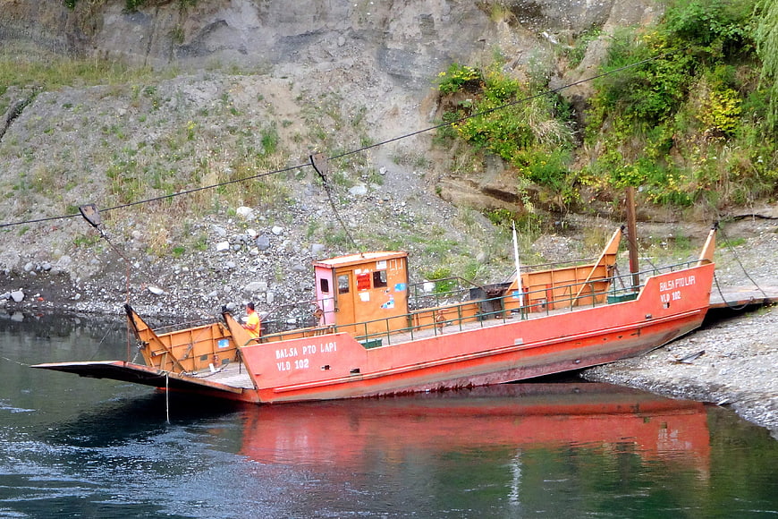 Orange cable ferry boat docked at rocky riverbank