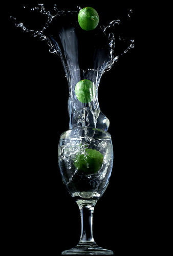 Limes splashing into a glass of water on a black background