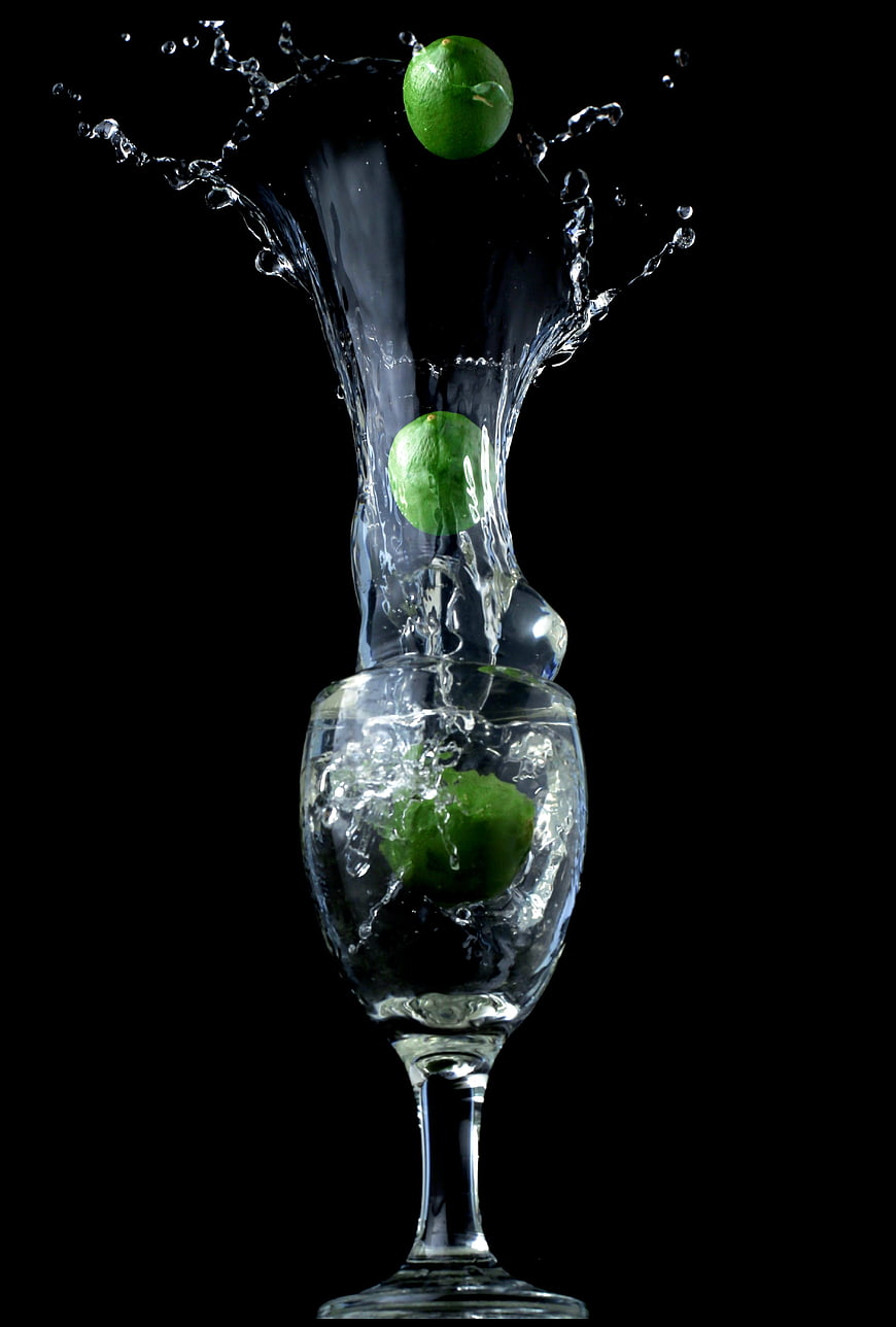Limes splashing into a glass of water on a black background