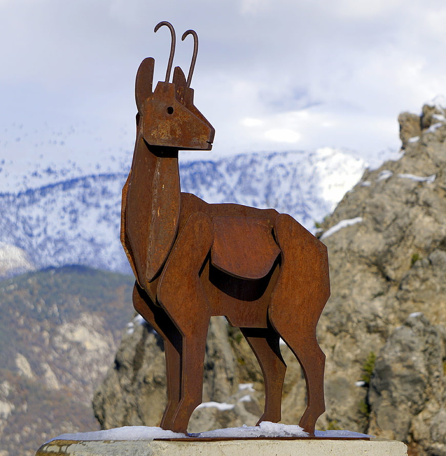 Rusty metal ibex sculpture against snowy mountain backdrop