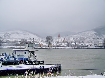 Snowy river landscape with docked barge and distant town