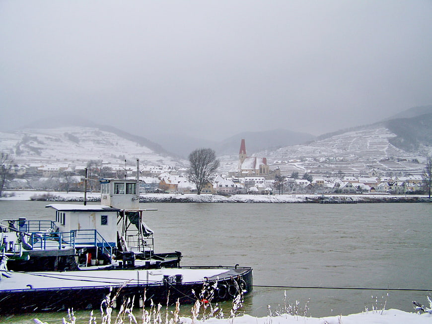 Snowy river landscape with docked barge and distant town