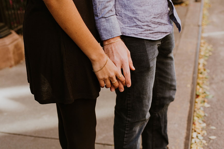 Couple holding hands with engagement rings on sidewalk