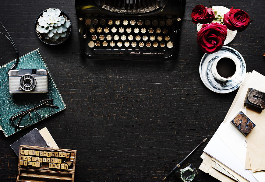 Vintage typewriter workspace with camera, roses, and coffee