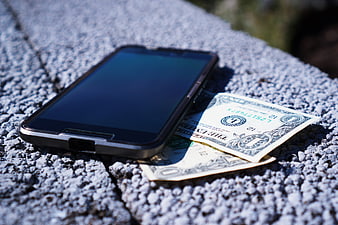 Smartphone and US Dollar Bills on Textured Concrete Surface