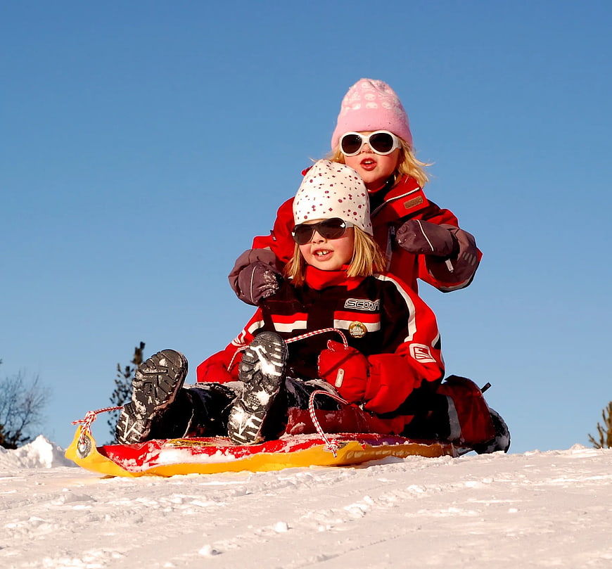 Two Girls Sledding Down Snowy Hill in Winter