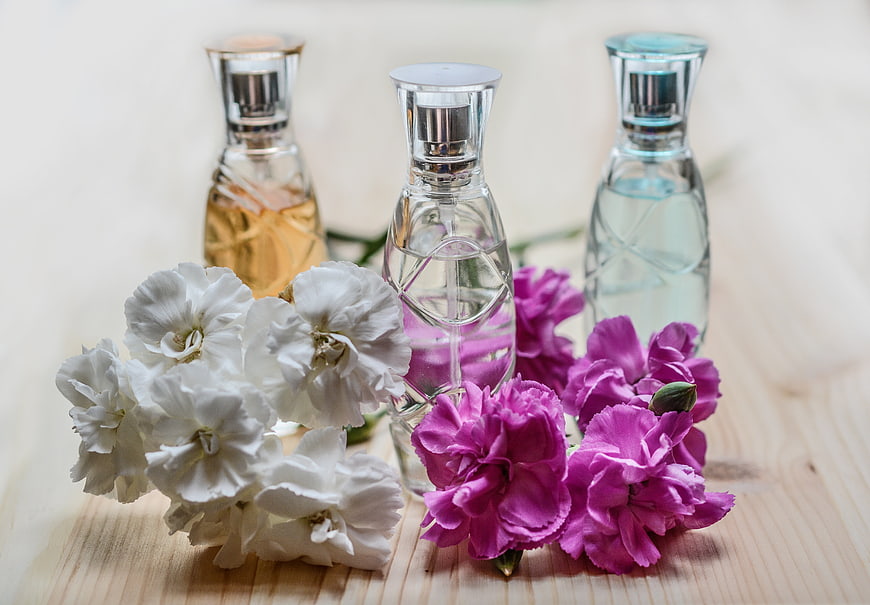 Perfume bottles with white and pink flowers on light wood