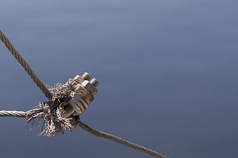 Close-up of frayed steel cable with metal clamp against blue background