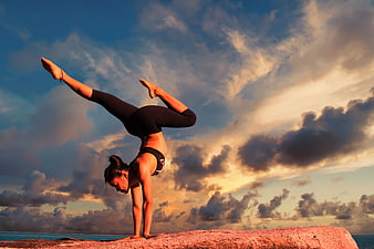 Woman performing yoga handstand on rock at sunset