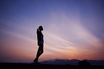 Silhouette of a woman walking against a colorful sunset sky