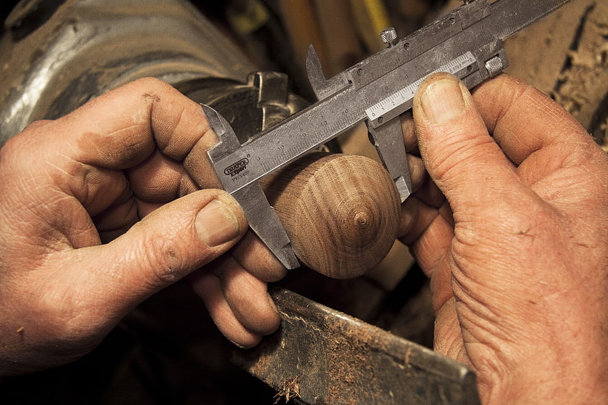 Carpenter Measuring Wood with Calipers in Workshop