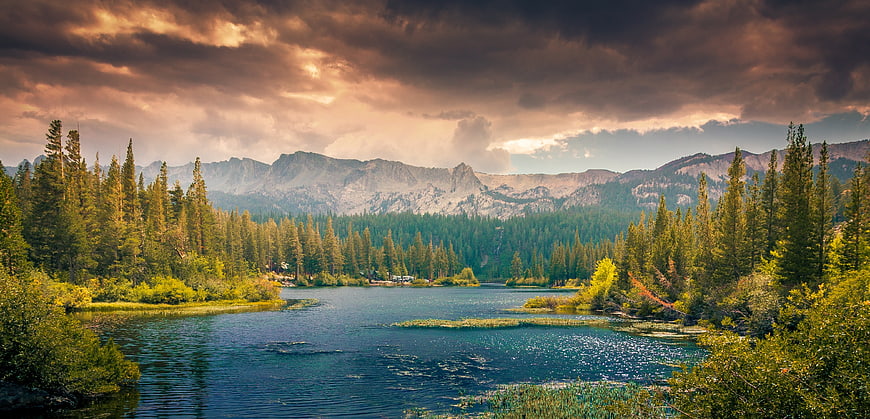 Dramatic sunset over mountain lake with pine forest