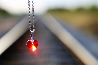 Red Heart Pendant Necklace Hanging Against Blurred Railway Tracks