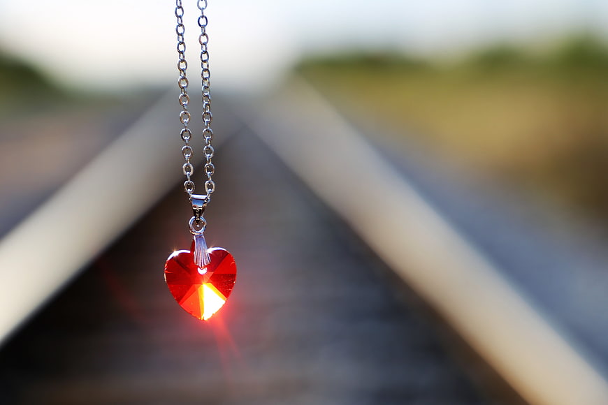 Red Heart Pendant Necklace Hanging Against Blurred Railway Tracks