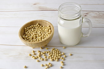Soybeans in wooden bowl and glass mug of soy milk on white wood
