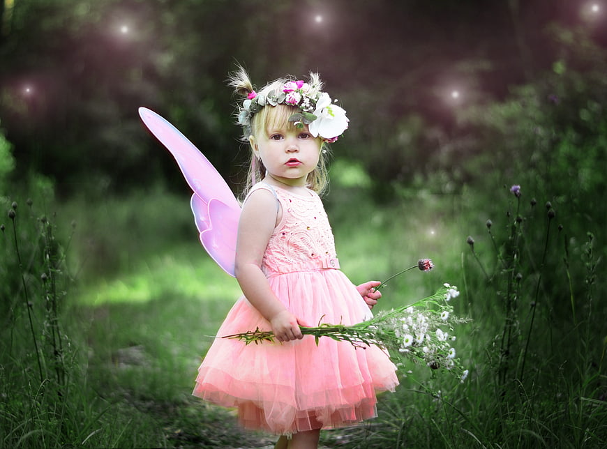 Little girl in pink fairy costume holding flowers in forest