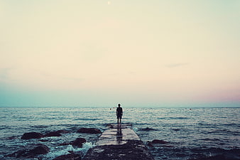 Man Standing on Pier Looking at Ocean at Sunset