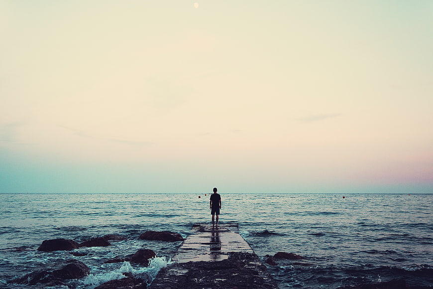 Man Standing on Pier Looking at Ocean at Sunset