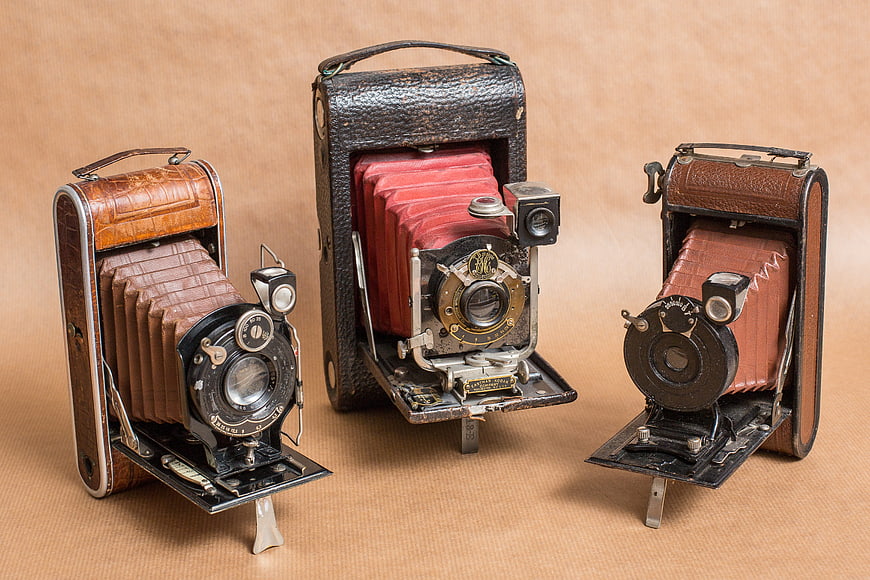 Three vintage folding cameras on beige background