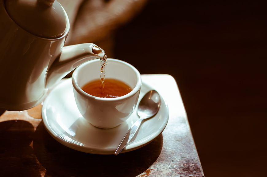 Pouring Hot Tea into White Cup on Wooden Table