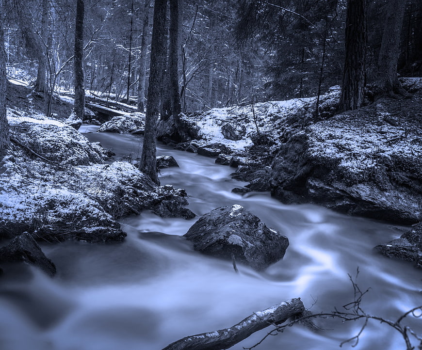 Long Exposure Winter Stream Flowing Through Snowy Forest
