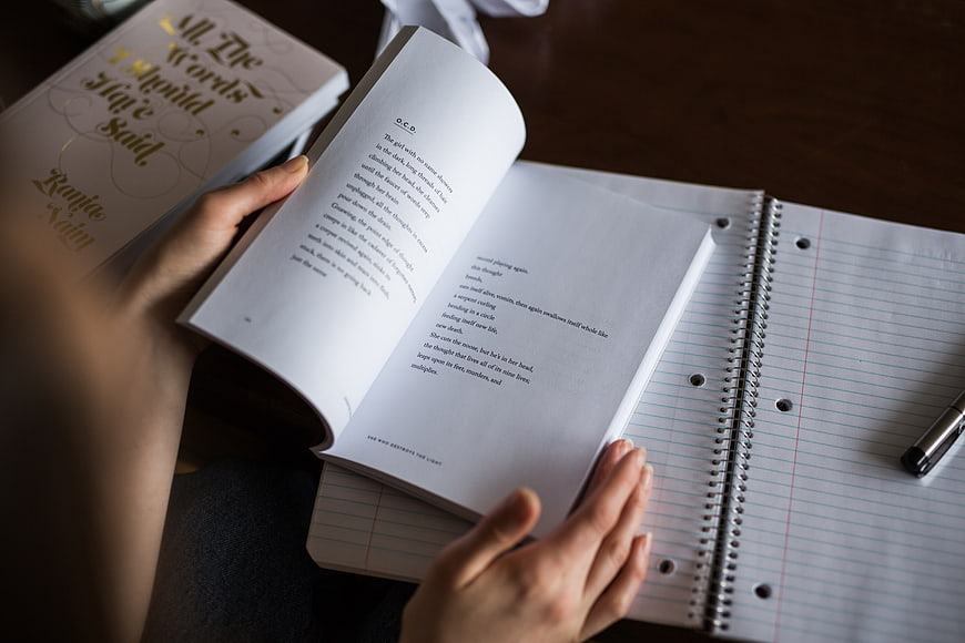 Hands holding open poetry book over notebook