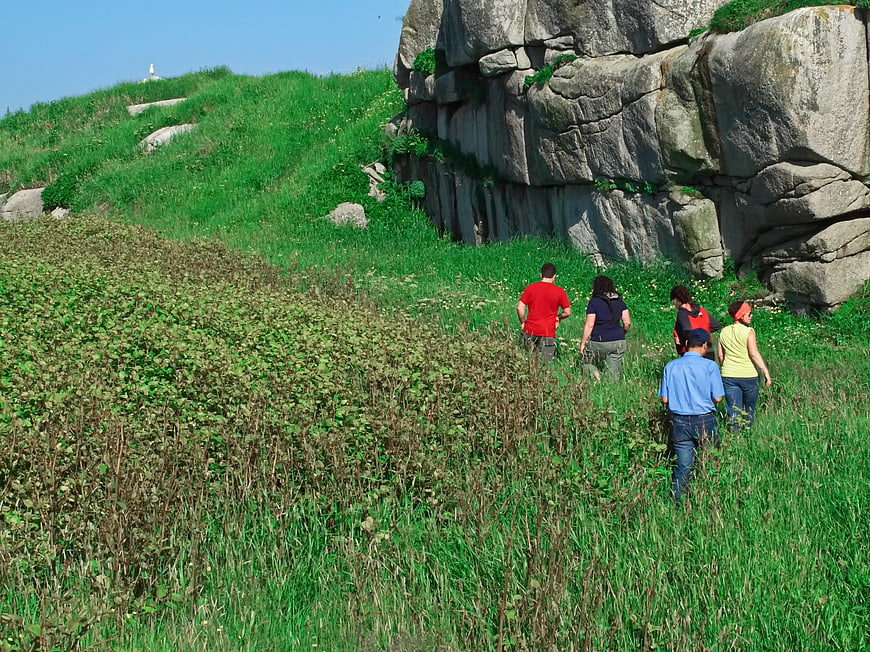 Group of Hikers Walking Through Green Field Near Rocks