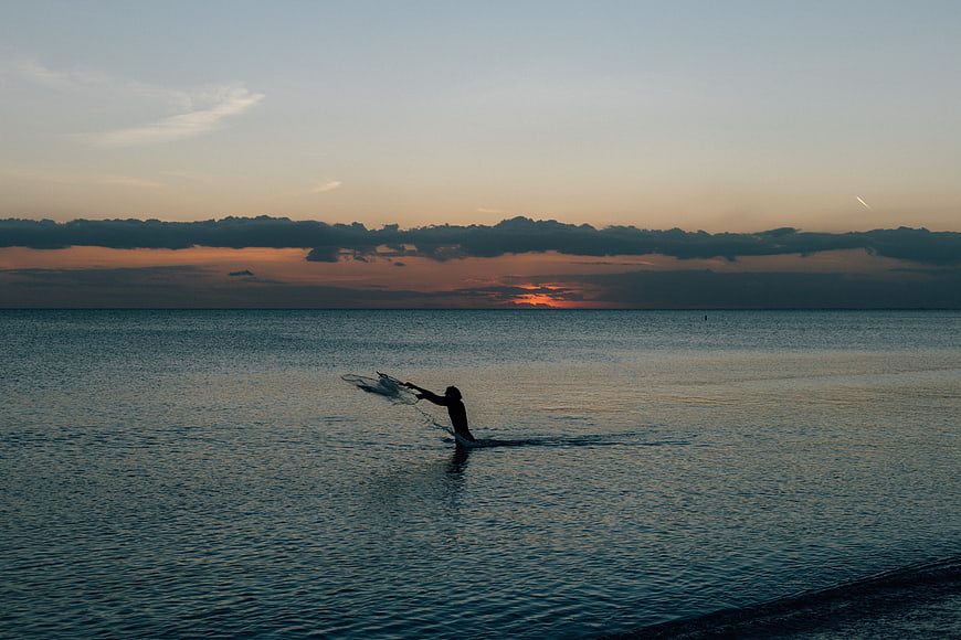 Silhouette of Fisherman Casting Net at Sunset Ocean