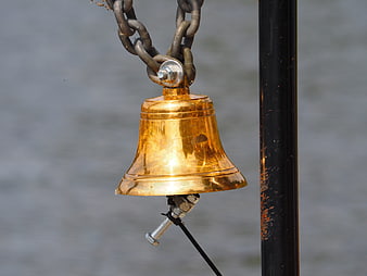 Close-up of a shiny brass bell hanging on a chain