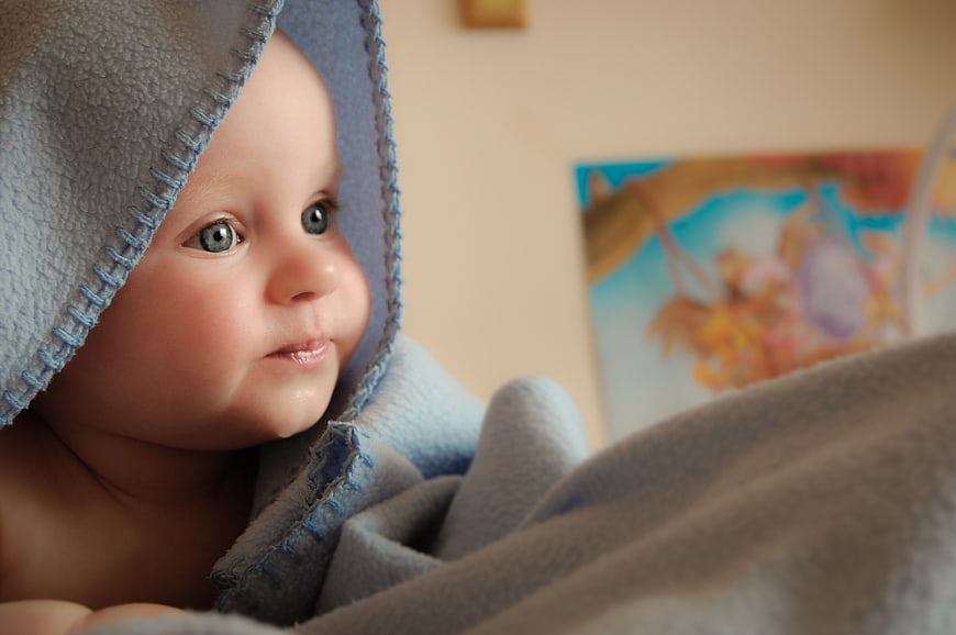 Cute baby wrapped in blue hooded towel looking at book