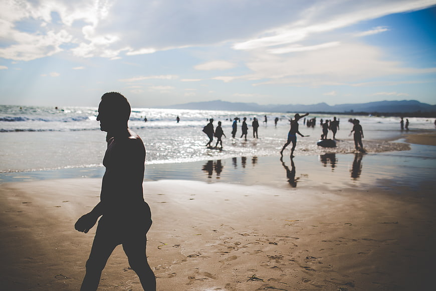 Silhouette of Man Walking on Beach with Crowd in Background