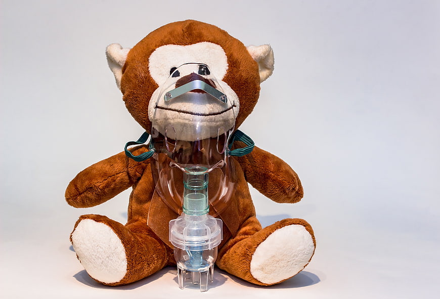 Teddy Bear Wearing Medical Nebulizer Mask on White Background