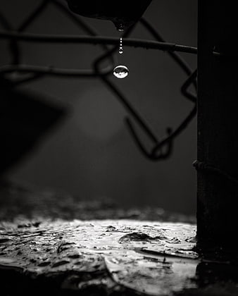 Black and white macro of water droplet falling from chain link fence