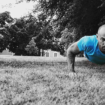 Man performing push-up on grass in selective color blue shirt