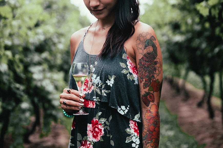 Woman with tattoos holding wine glass in vineyard