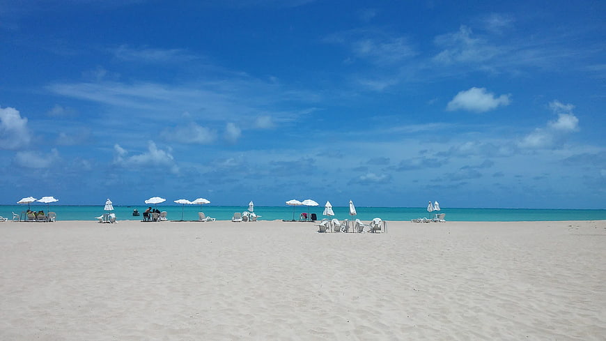 Wide shot of white sand beach with turquoise water and blue sky