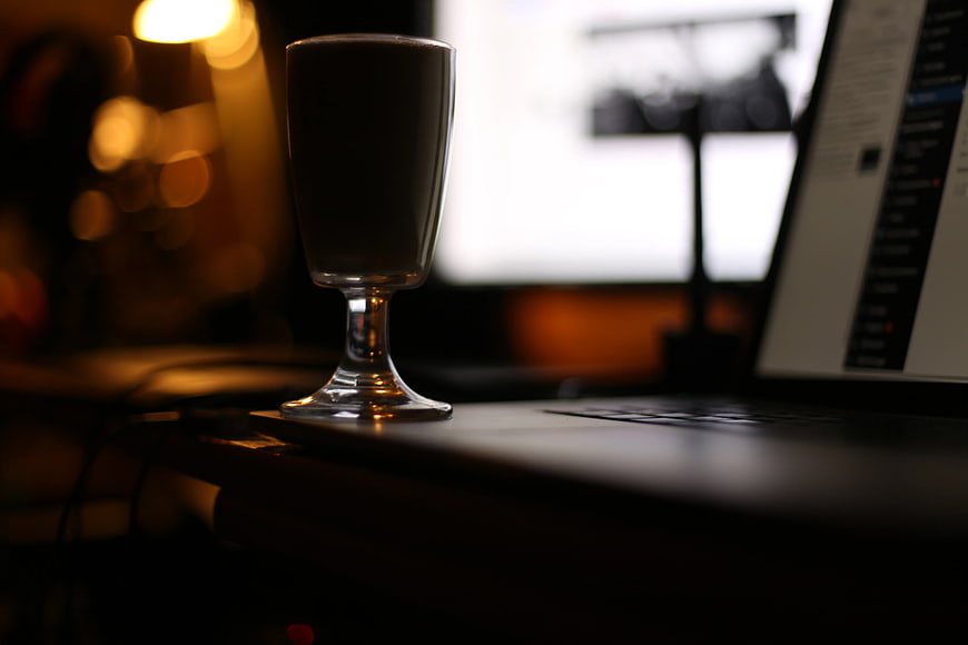 Glass of dark drink on laptop keyboard at night