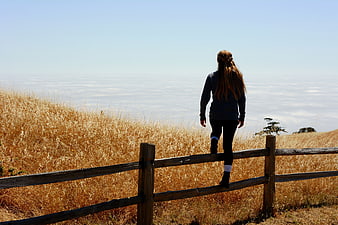 Woman climbing wooden fence overlooking sea of clouds