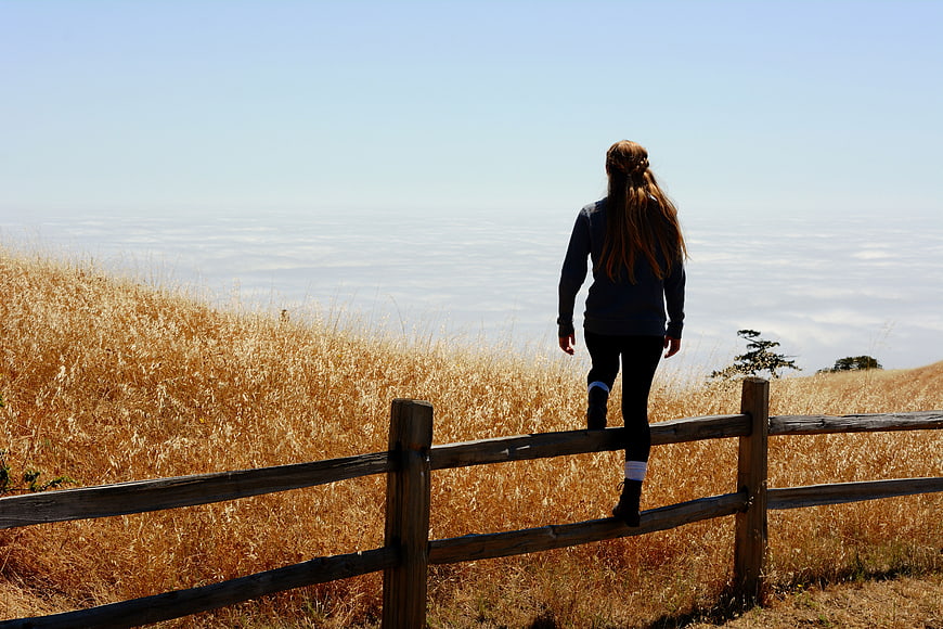 Woman climbing wooden fence overlooking sea of clouds
