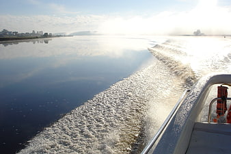 Boat wake on calm river with morning mist and sunlight