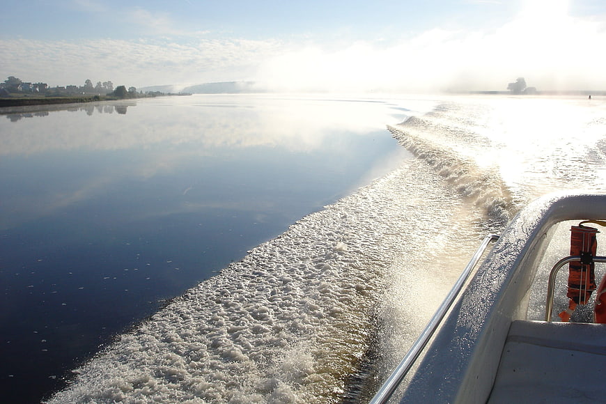 Boat wake on calm river with morning mist and sunlight