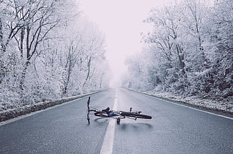 Fallen bicycle on empty winter road in snowy forest